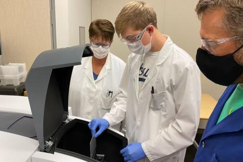 Connor Mosebey (center) loads a materials sample into a UV-Vis spectrometer 