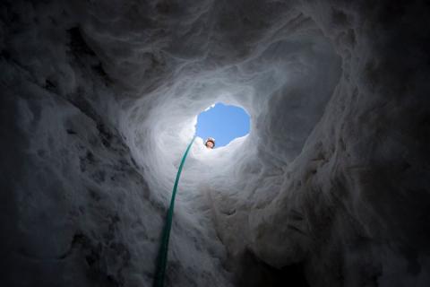 Penn State graduate student Kiya Riverman looks down a shaft into a cave inside a glacier in Norway's Svalbard region.