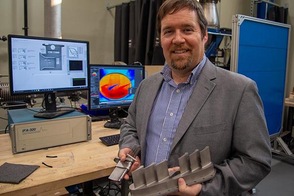 Stephen Lynch, associate professor of mechanical engineering, holds metal 3D-printed turbine vanes 