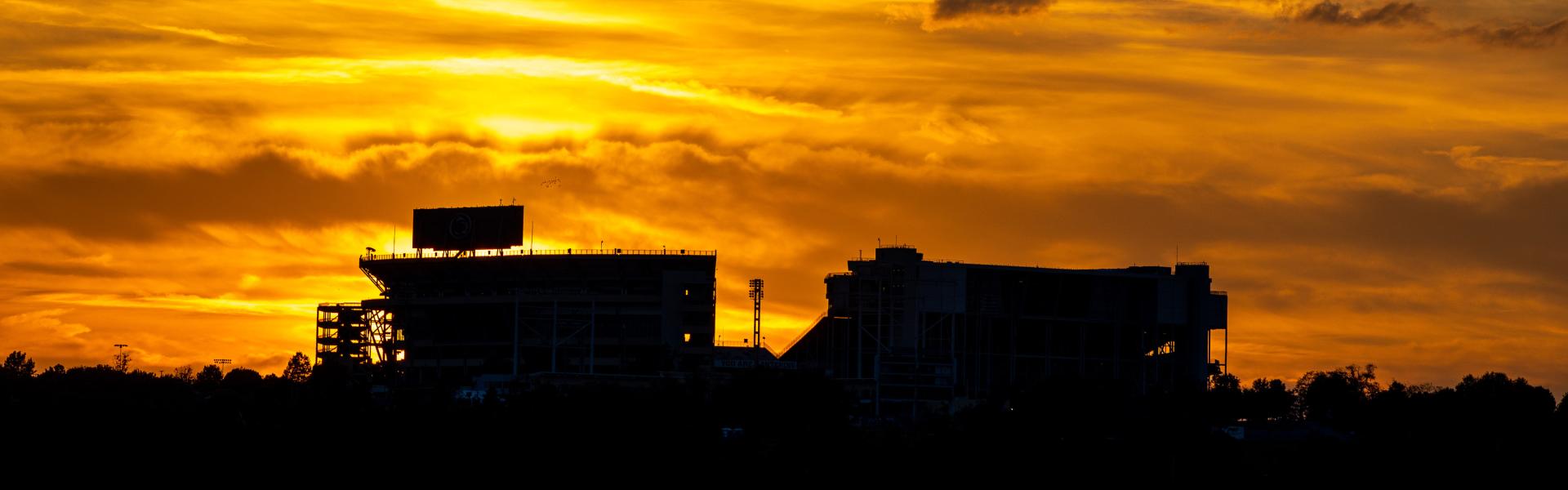 beaver stadium with the sun setting and glowing orange in the background